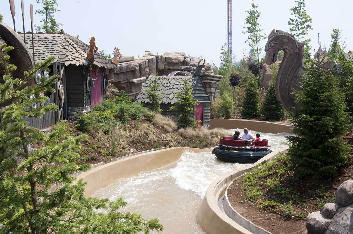 Οι άνθρωποι σε μια σχεδία περνούν μέσα από ένα στριφογυριστό υδάτινο ρεύμα, που περιβάλλεται από καταπράσινο τοπίο, ρουστίκ κτίρια και πέτρινες κατασκευές.