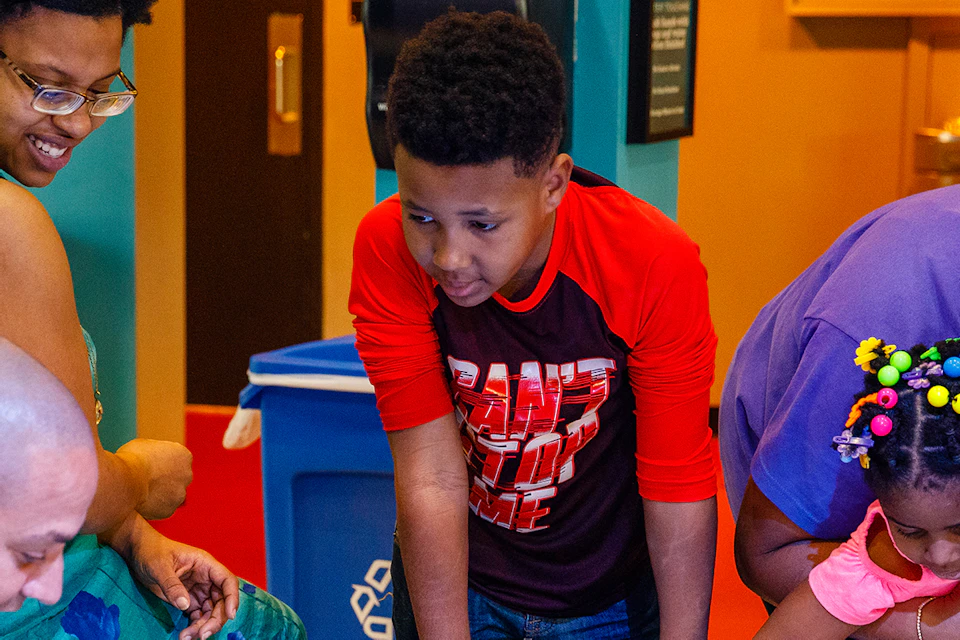 Adults and children interact with sea creatures in a touch pool at an indoor aquarium, looking curious and engaged.