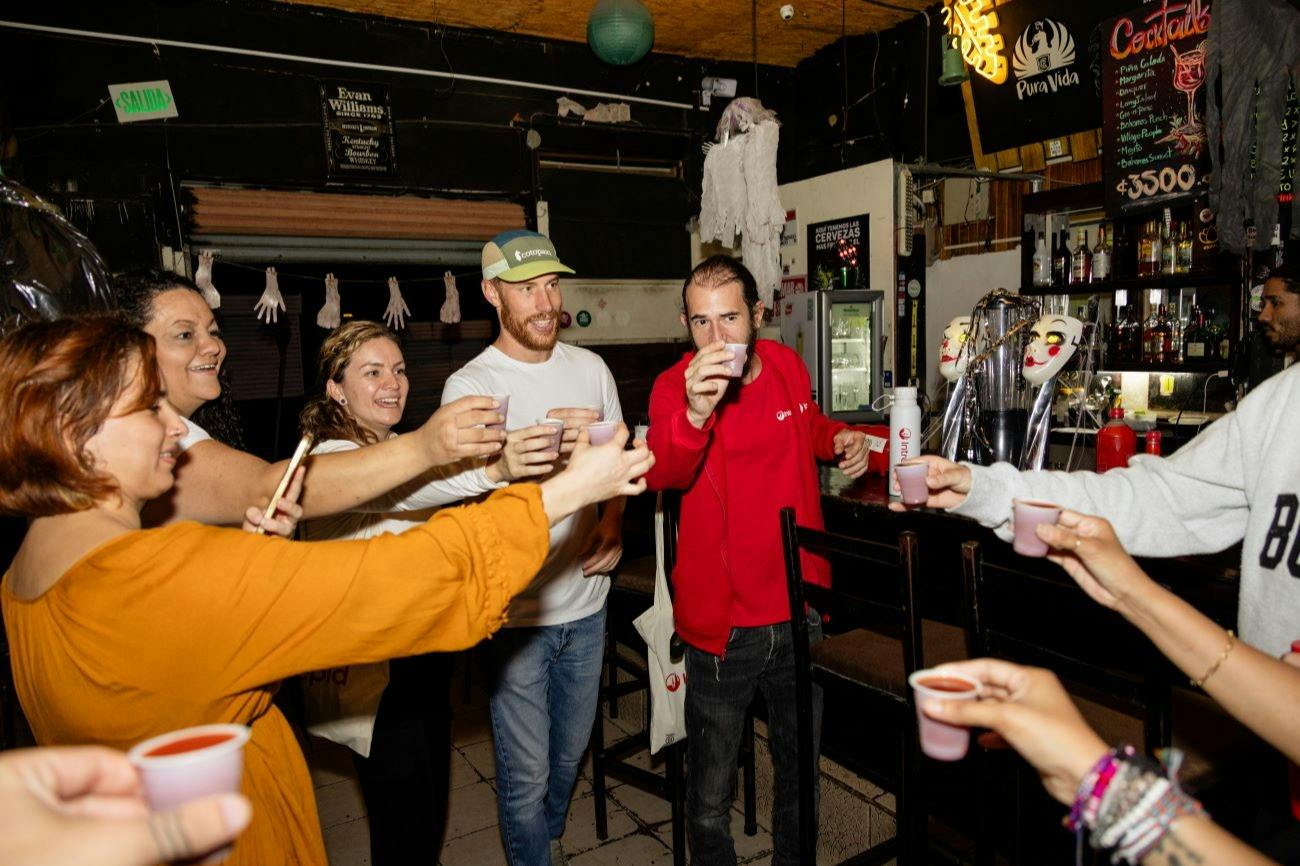 A group of people raising small cups together in a toast inside a casual setting.