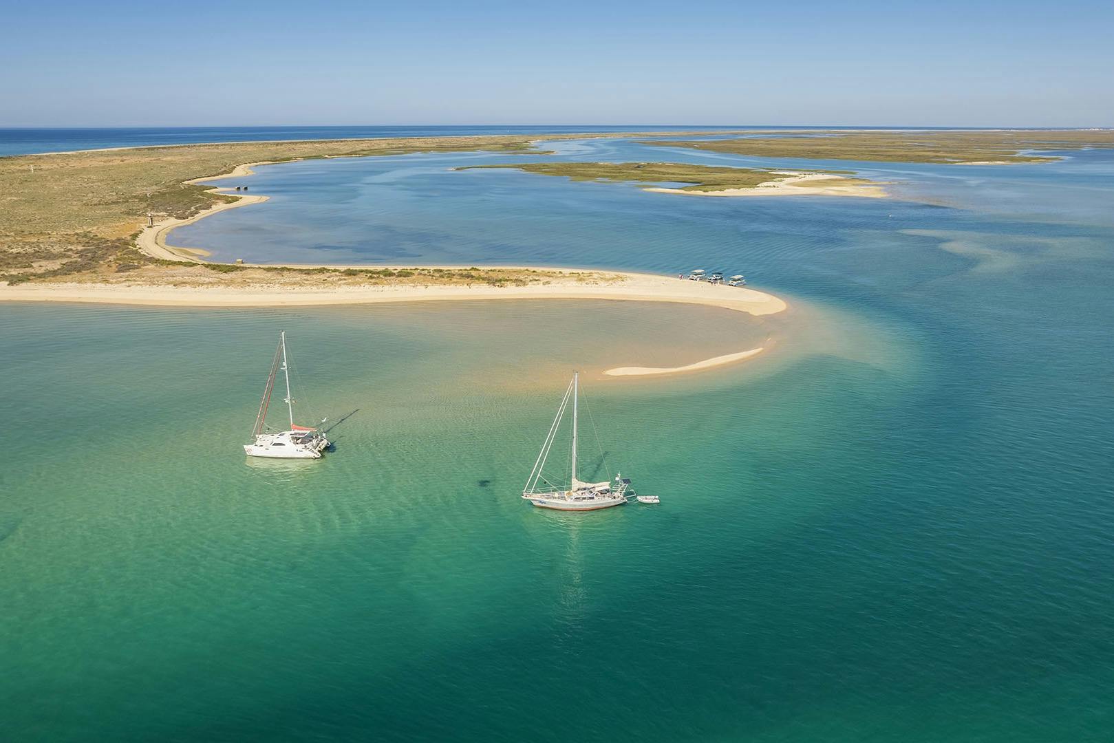 Парусники стоят на якоре рядом с островом Дезерта с прозрачной бирюзовой водой, окруженной прибрежными заливами и спокойным открытым морем.