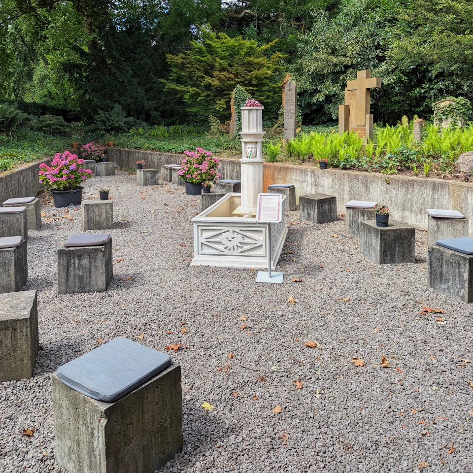 A small outdoor chapel with stone benches arranged in a semicircle around a white stone altar, surrounded by greenery.
