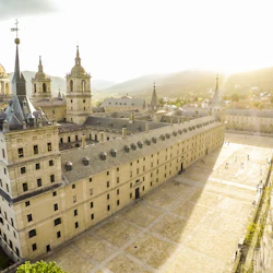 Flygfoto över ett stort historiskt stenbyggnadskomplex med torn och en innergård i sen eftermiddagssol.