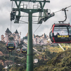 Cable cars with "Sun World" branding travel above lush greenery, with a castle-like structure in the background.