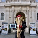Person in a Leonardo da Vinci costume holding a tablet in front of a historic building with