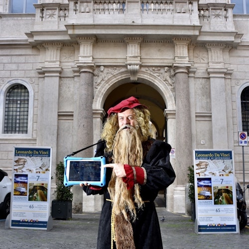 Person in a Leonardo da Vinci costume holding a tablet in front of a historic building with
