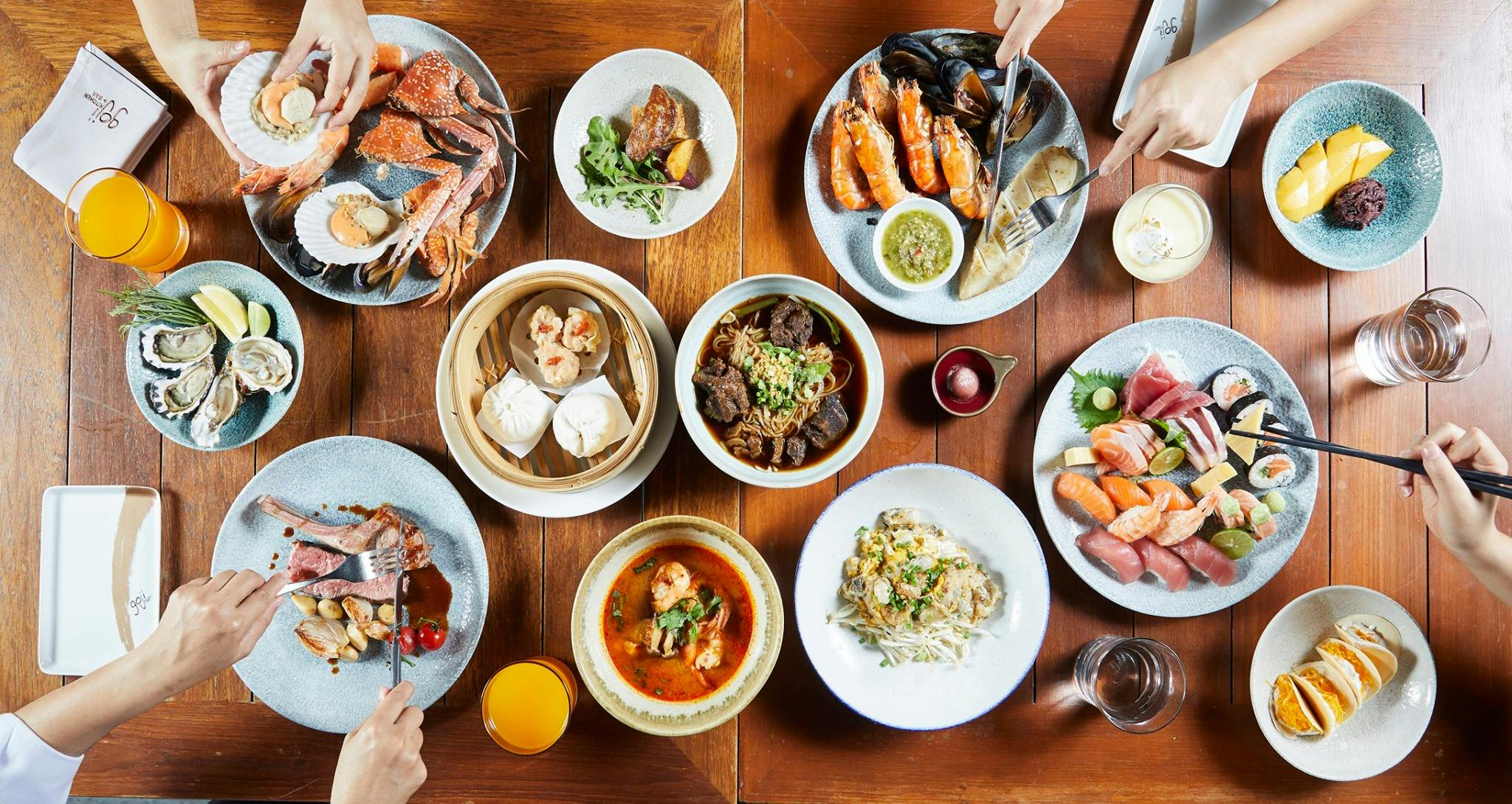 A table set with various dishes of Asian and Western cuisines, including seafood, noodles, dim sum, and sushi.