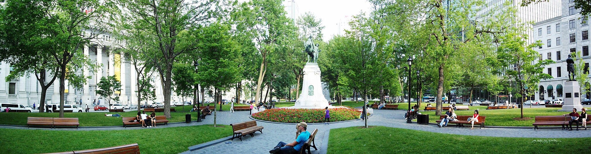 市中心有雕像的城市公园，四周环绕着树木、长凳，人们坐着或走着。