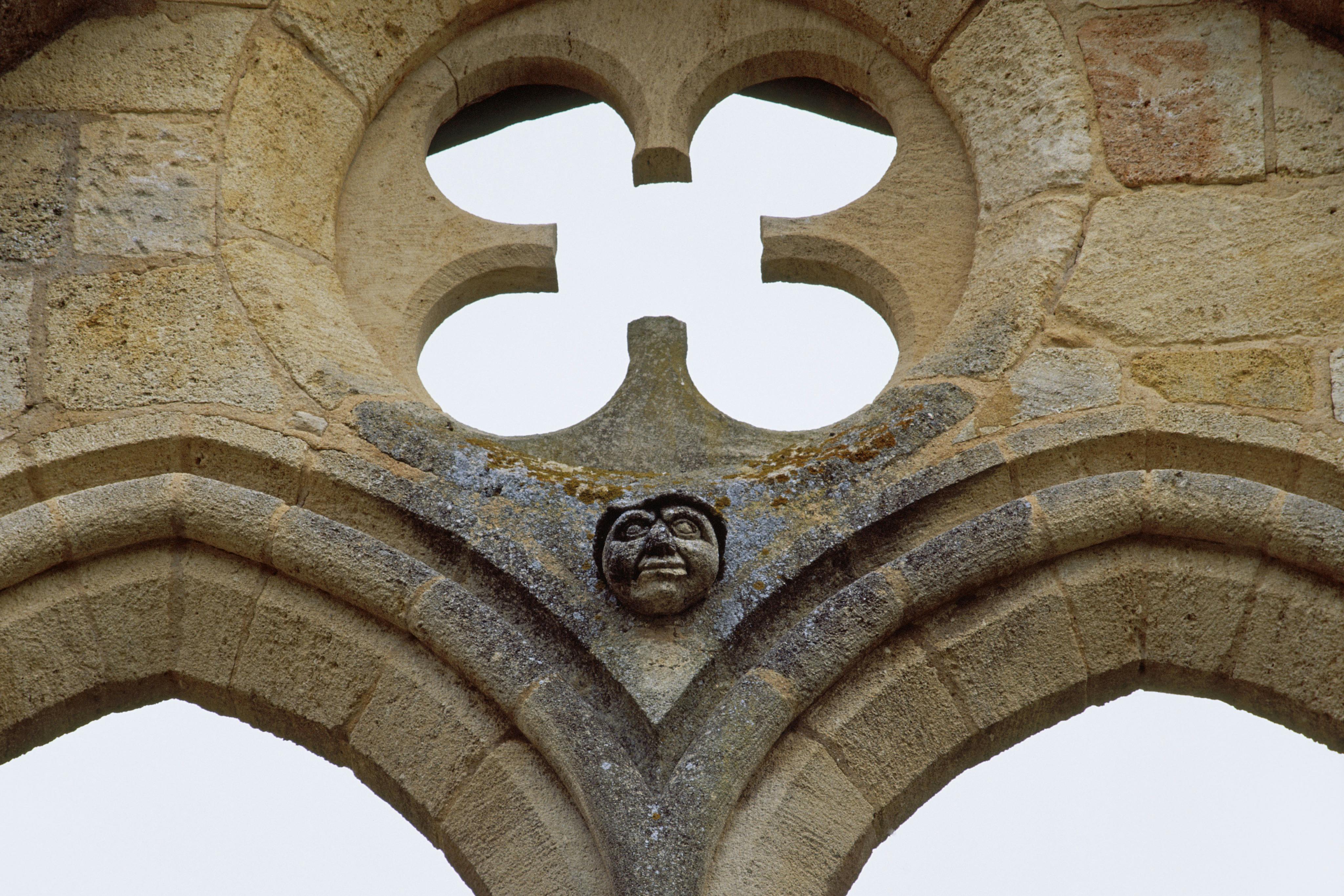 Μια σκαλιστή πέτρινη αψίδα με πρόσωπο στο κέντρο και τετράφυλλο άνοιγμα από πάνω της.