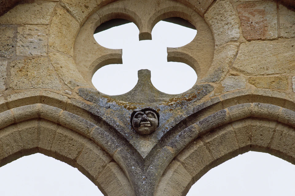 A carved stone arch with a face at the center and a quatrefoil opening above it.