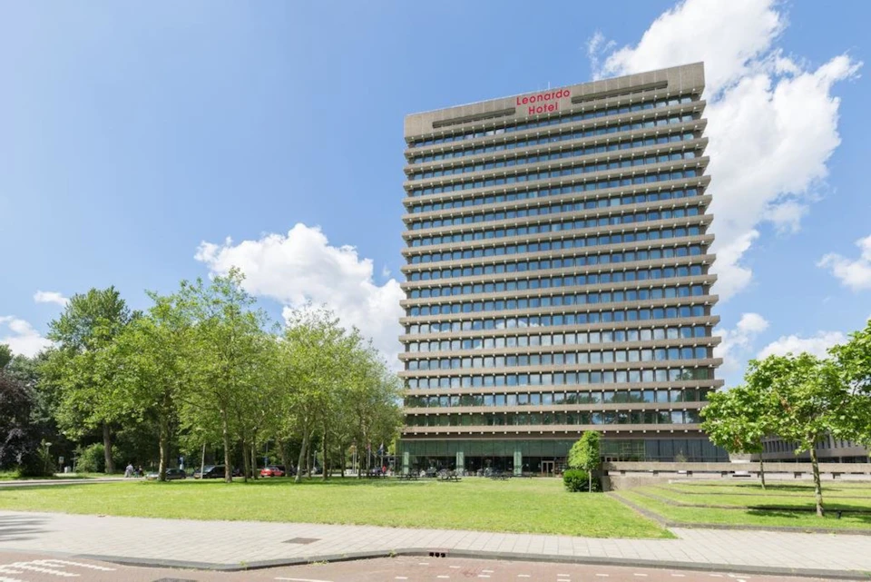 A tall building labeled "Leonardo Hotel," surrounded by grass, trees, and a blue sky with clouds.