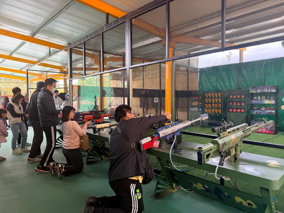 People aiming rifles at a shooting range with targets in the background, in an indoor facility with green flooring.