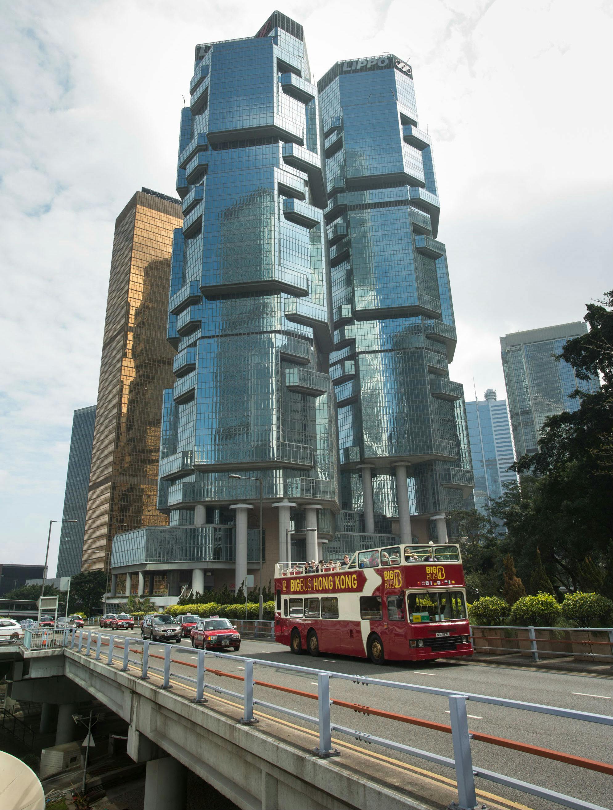近代的なガラス張りの高層ビルやその他の車両が並ぶ街並みの道路を走る赤い二階建てバス。
