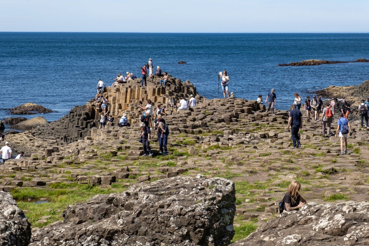 Des touristes explorent la Chaussée des Géants, une formation rocheuse naturelle en bord de mer, sous un ciel bleu limpide.