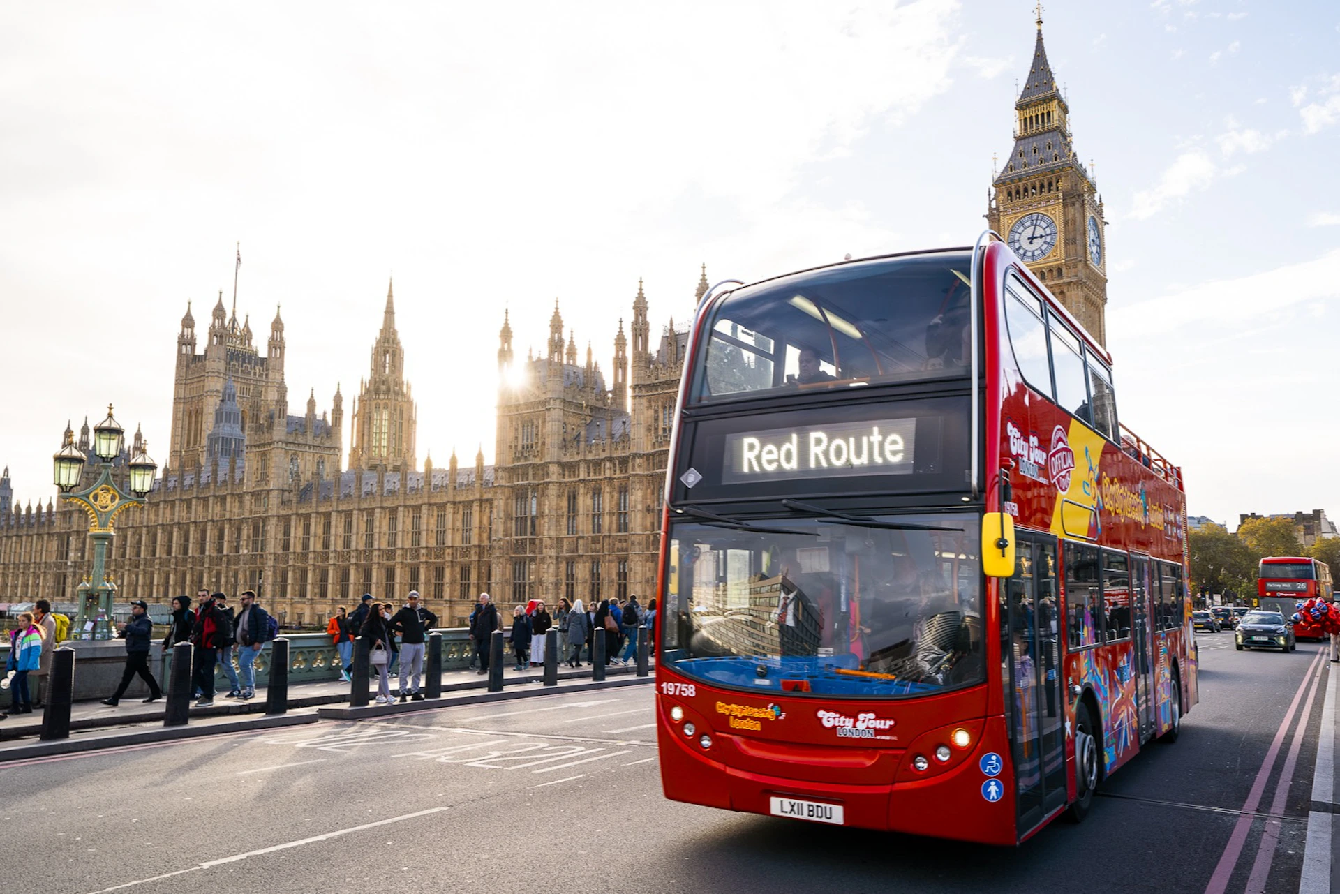 A red double-decker tour bus on a street near the Houses of Parliament and Big Ben in London.