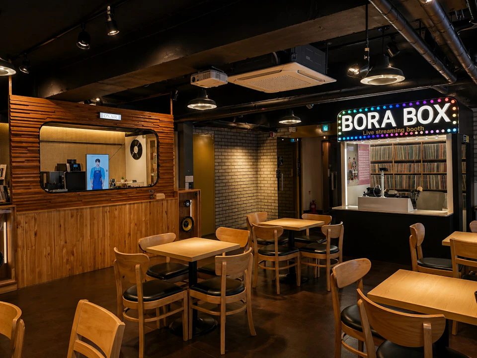 Interior of a cozy cafe or bar with wooden tables and chairs, a bar counter, and a sign reading 'Bora B.'