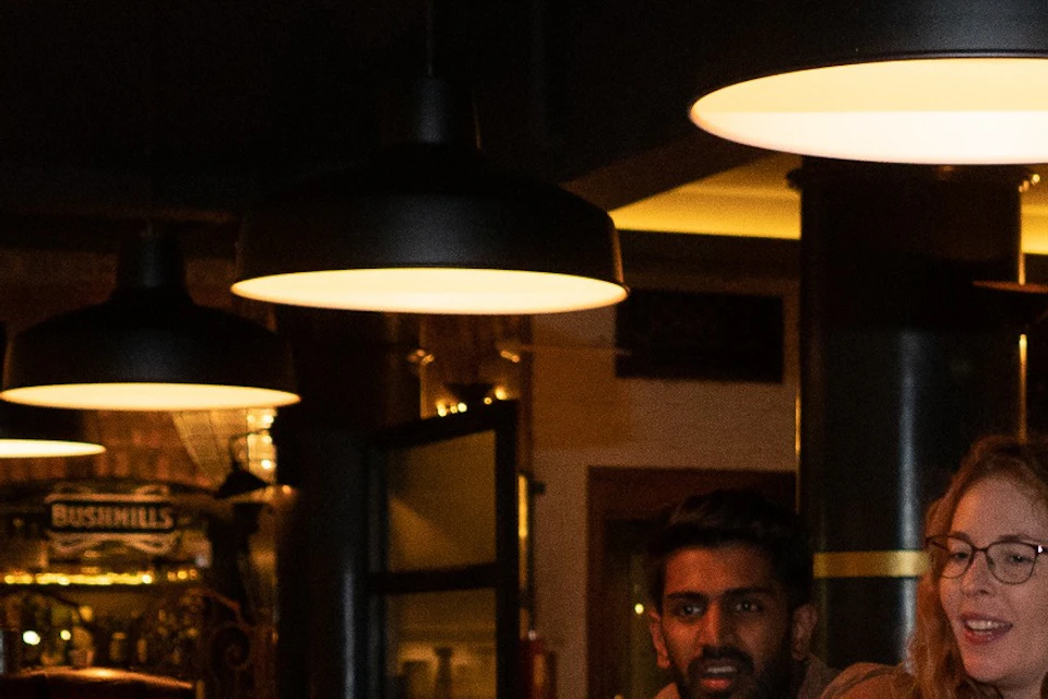 A bartender pouring a liquid into a jigger, with a cocktail glass and bar equipment on the counter in a dimly lit bar.