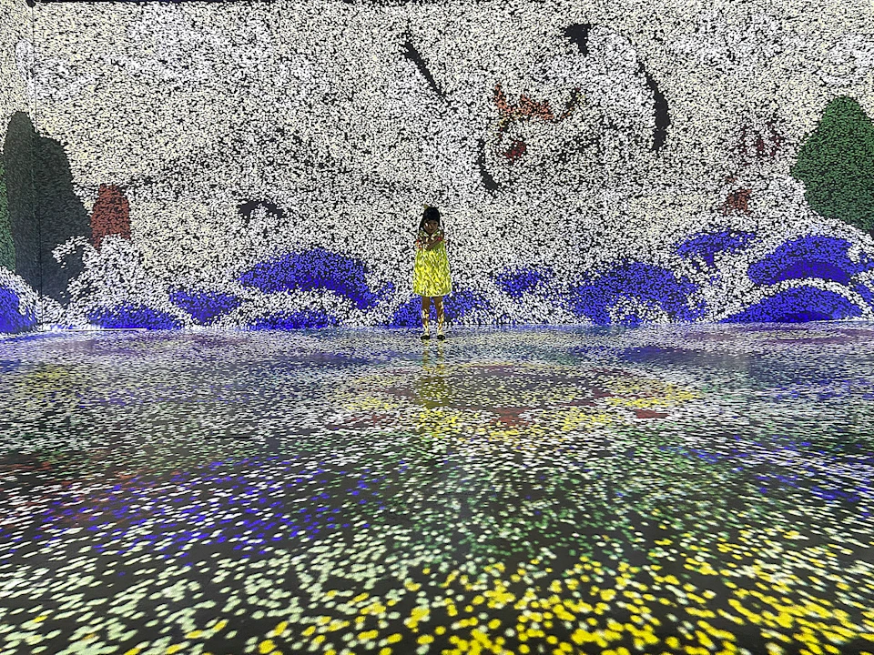 A person in a yellow dress stands in a space with walls and floor covered in colorful, pixel-like patterns.