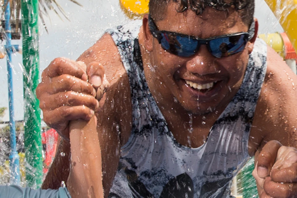A man and two children run through water jets under colorful hoops at a water park, all wearing swimwear and smiling.