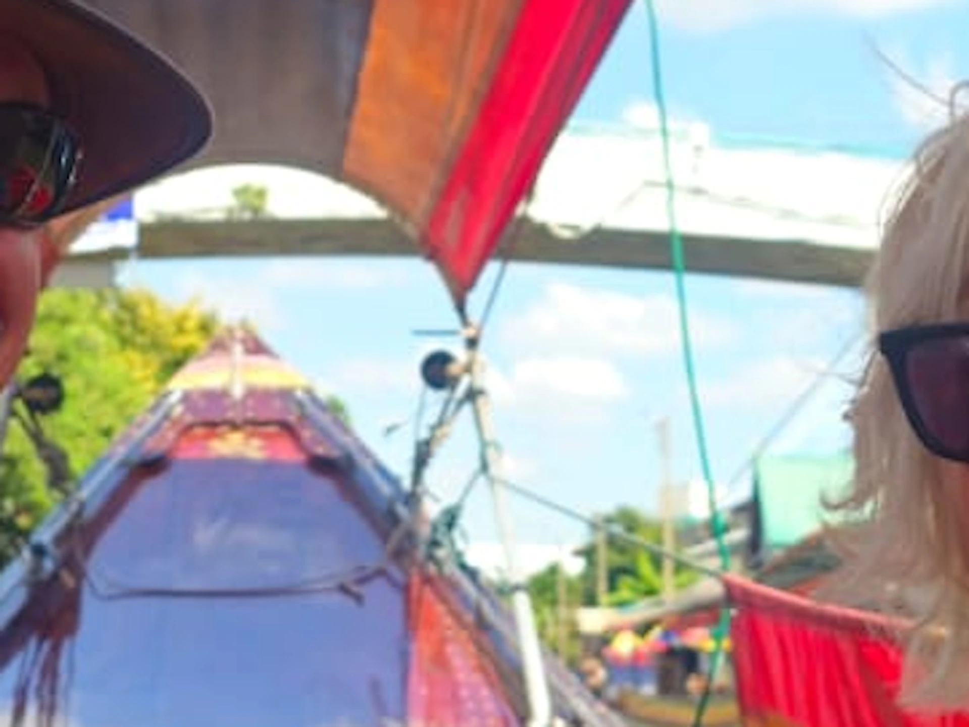 A man and woman sitting on a boat with colorful tarpaulin, with a large golden statue and buildings visible in the background.