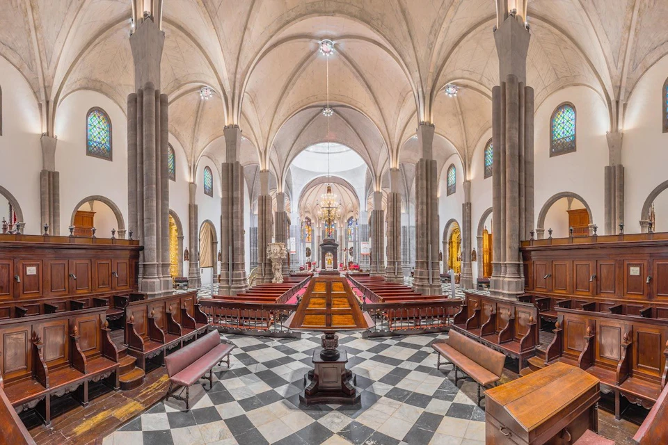 Interior of a grand church with vaulted ceilings, ornate details, and symmetrical seating arrangements.
