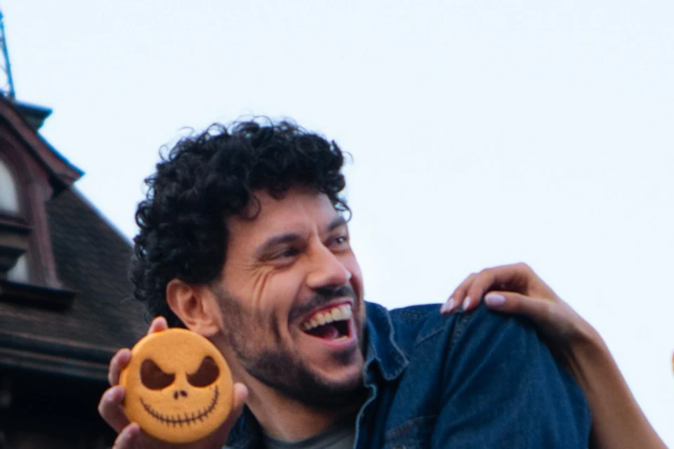 Three people enjoy a Halloween-themed setting near a decorated building with pumpkins and autumn leaves.