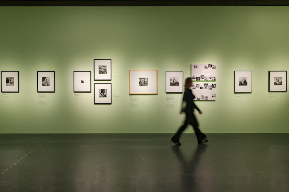 A person walks past a gallery wall displaying framed black-and-white photographs on a light green background.