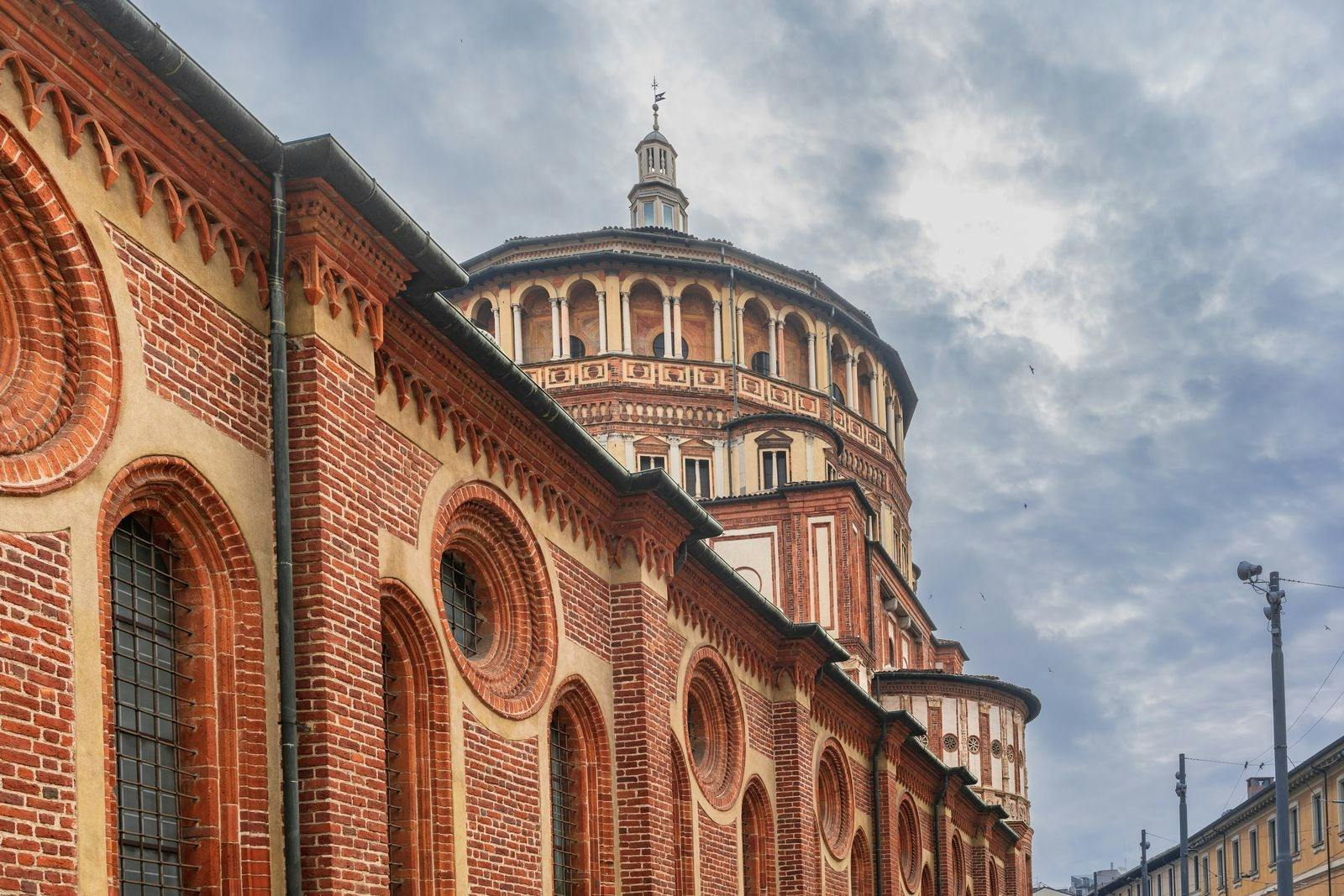 Brick and stone church with arched windows and a dome against a cloudy sky.