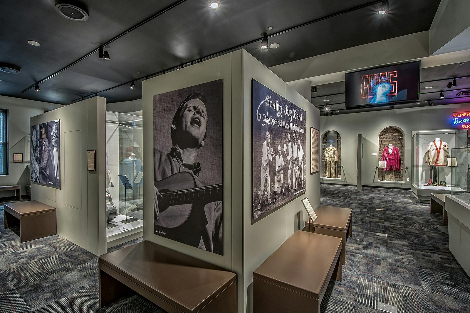 Museum exhibit with large photographs of musicians, informational plaques, glass display cases, and brown benches.