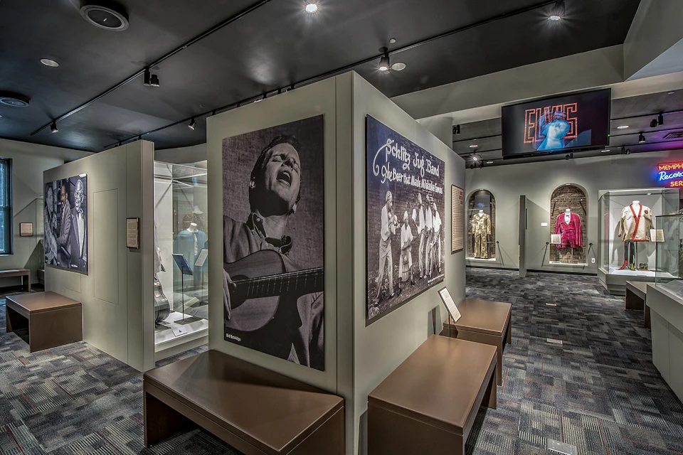 Museum exhibit with large photographs of musicians, informational plaques, glass display cases, and brown benches.