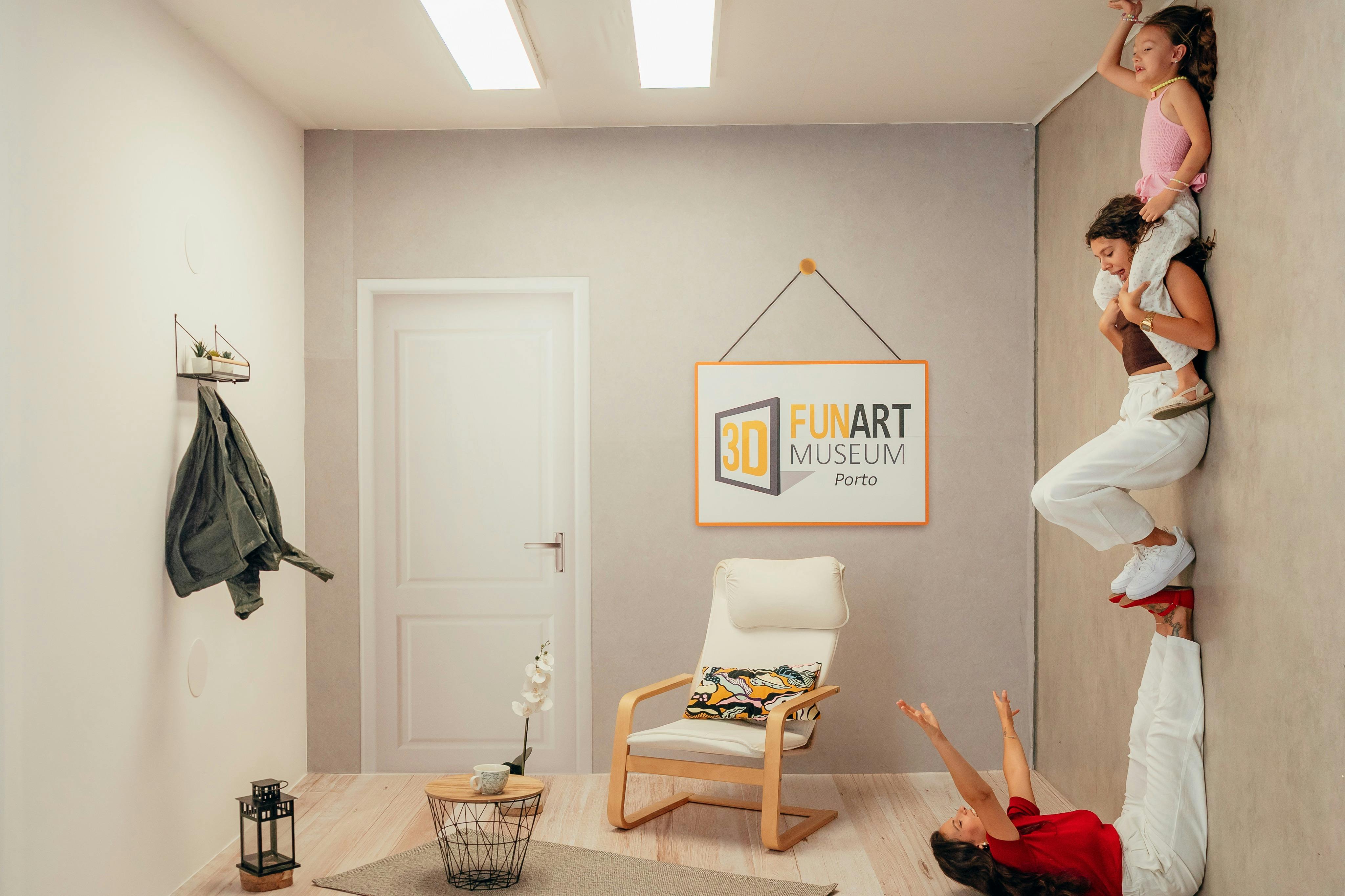 Une femme est allongée sur le sol, tenant une autre femme debout sur ses mains, qui porte un enfant dans une salle de musée avec un panneau "3D FUN ART MUSEUM Porto".