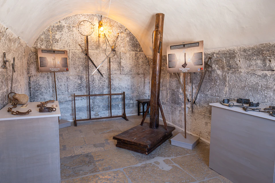 A small historical exhibit room with old metal tools on display, an upright wooden structure, and informational signs on the walls.