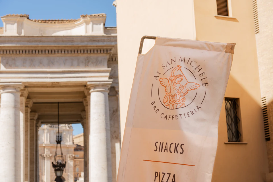 A sign for 'Al San Michele Bar Caffetteria' with visible snacks and pizza text, set in a sunny architectural setting.