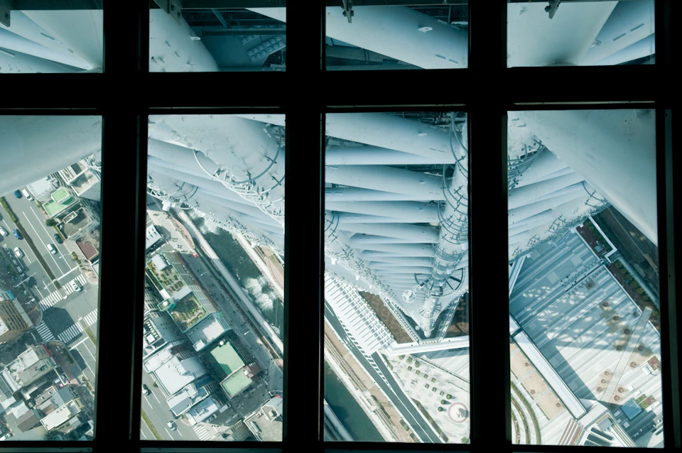 View through a glass floor showing the base of a tall structure and surrounding roads and buildings from a high vantage point.