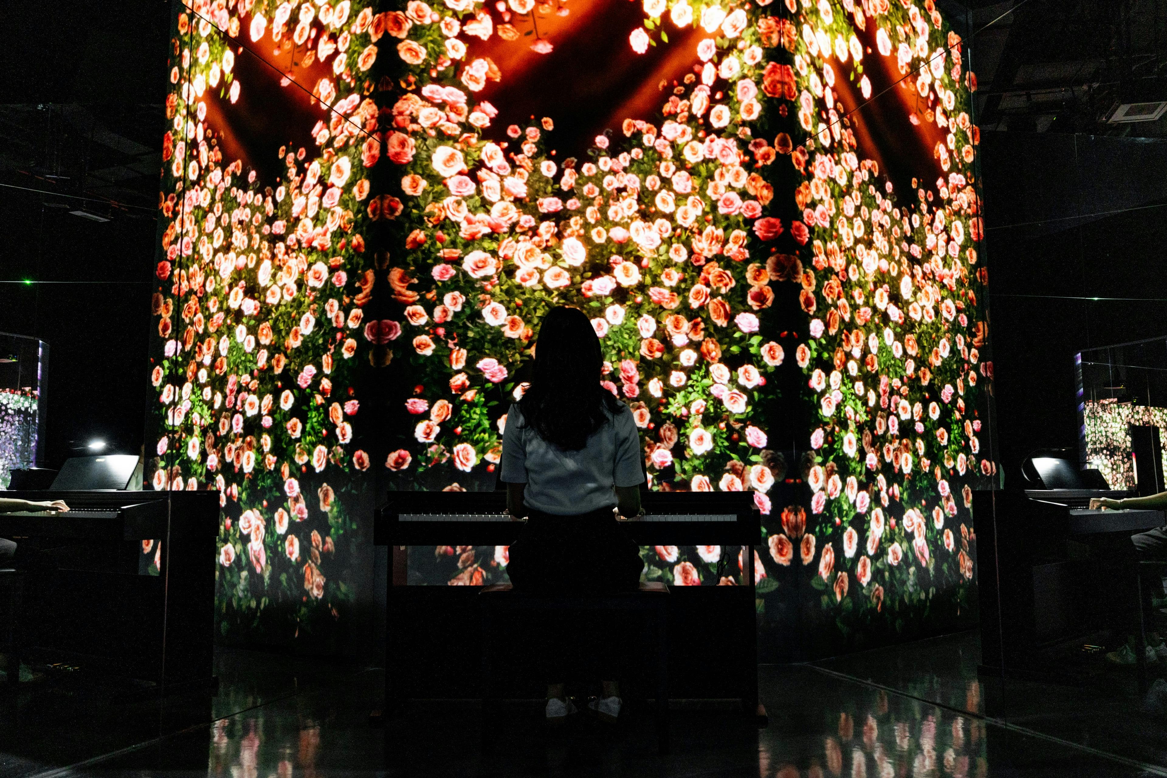 Osoba siedząca przy klawiaturze przed dużą, wciągającą kwiatową ekspozycją licznych oświetlonych kwiatów.