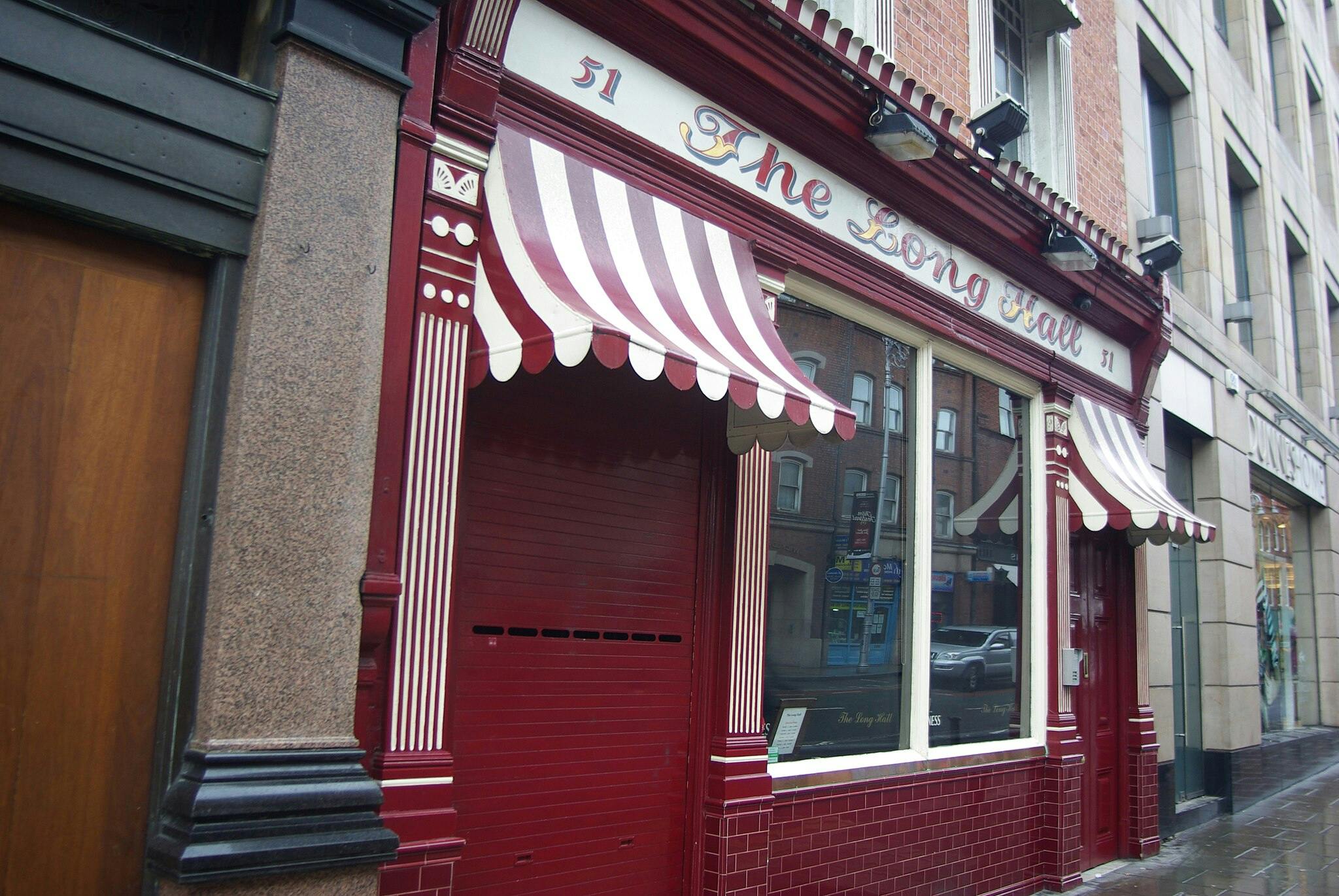 A storefront with red and white striped awnings, a red facade, large window, and the name "The Long Hall" displayed above.
