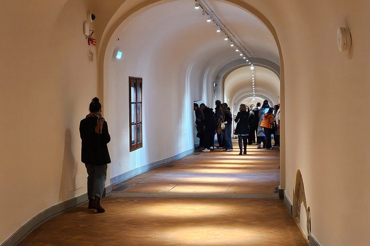 遠くの端に集まった人々のグループと、左側の壁に独りで立っている一人の人物がいる、長いアーチ型の廊下。