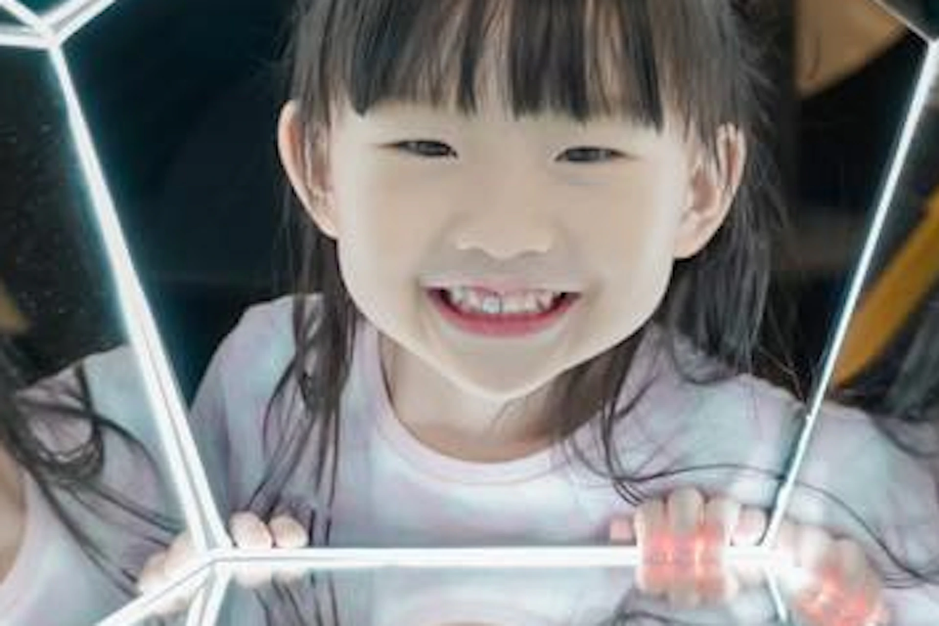 A child is smiling inside a pentagon-shaped mirror structure, creating multiple reflections of the child within.