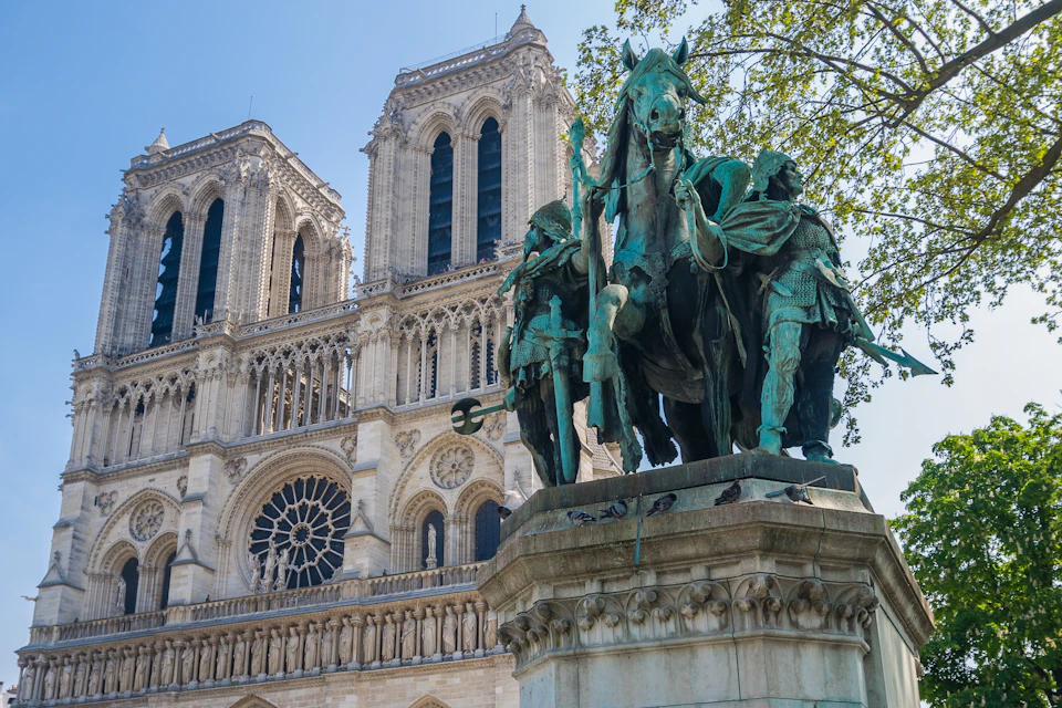 Statue of a historic figure on horseback in front of Notre-Dame Cathedral, with detailed architecture and leafy green trees.