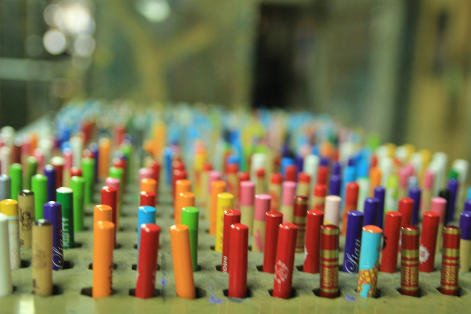 Colorful cylindrical objects arranged upright in a grid on a perforated surface, with a blurred background.