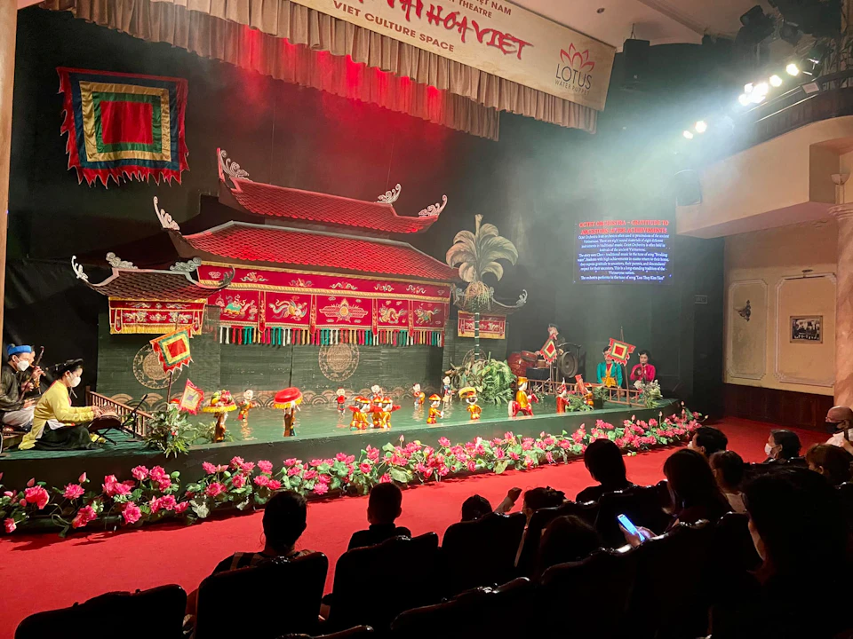 A traditional Vietnamese water puppet performance on a stage, viewed by an audience in a theater.