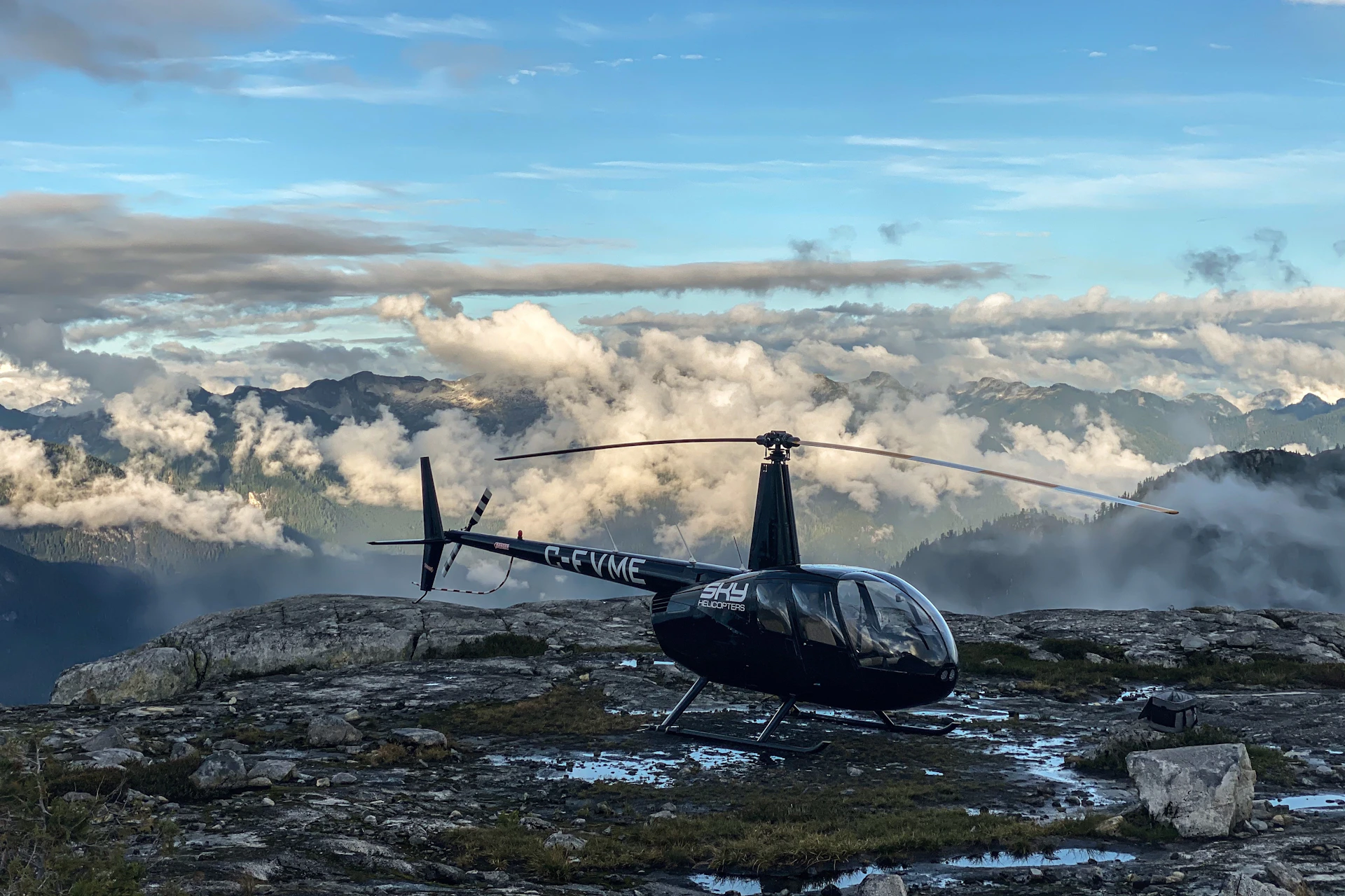 A helicopter landed on a mountain with mountain views in the background.