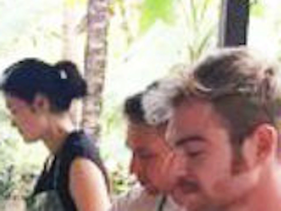 People in aprons cooking at outdoor stations with pots and pans, surrounded by lush greenery.