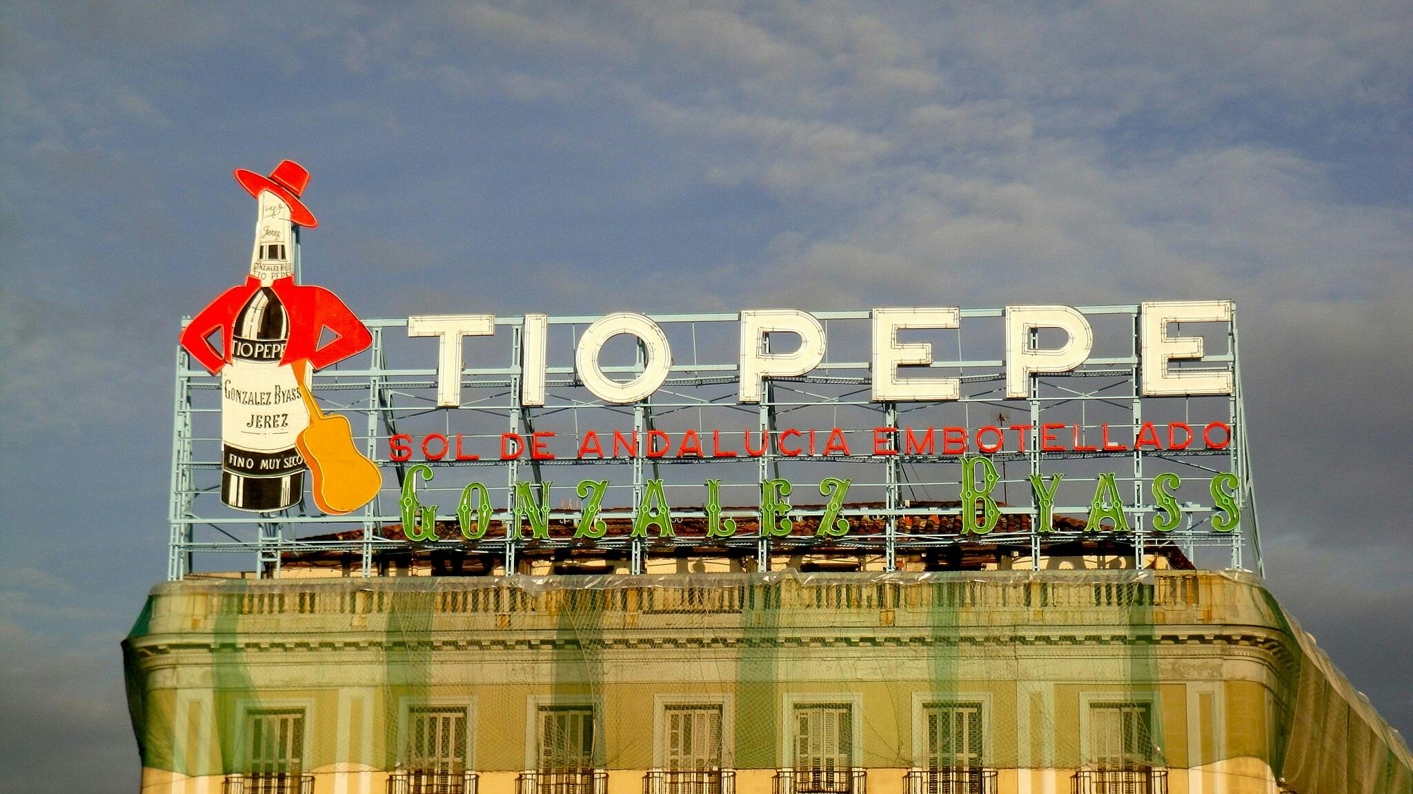 Large neon sign on a building with “Tio Pepe” and a bottle wearing a red jacket and hat, holding a guitar.