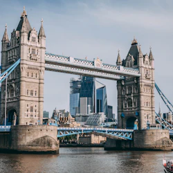 Tower Bridge över Themsen med Londons moderna skyline i bakgrunden, och en båt i förgrunden.