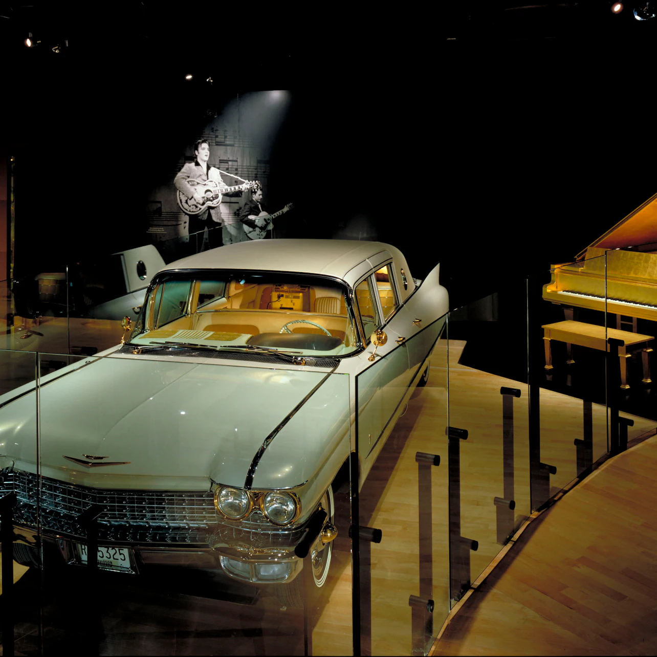 Exhibit featuring a vintage car, a grand piano to the right, and a photo of a musician with a guitar in the background.