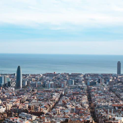 Flygfoto över en tät stad med flera skyskrapor nära kusten, under en delvis molnig himmel.