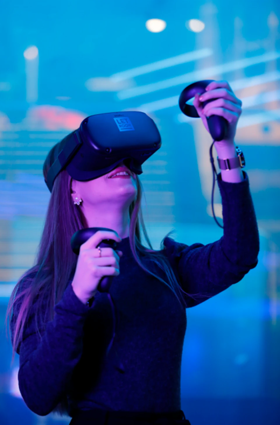 A woman wearing a VR headset and holding controllers, smiling while looking upwards in a blue-lit environment.