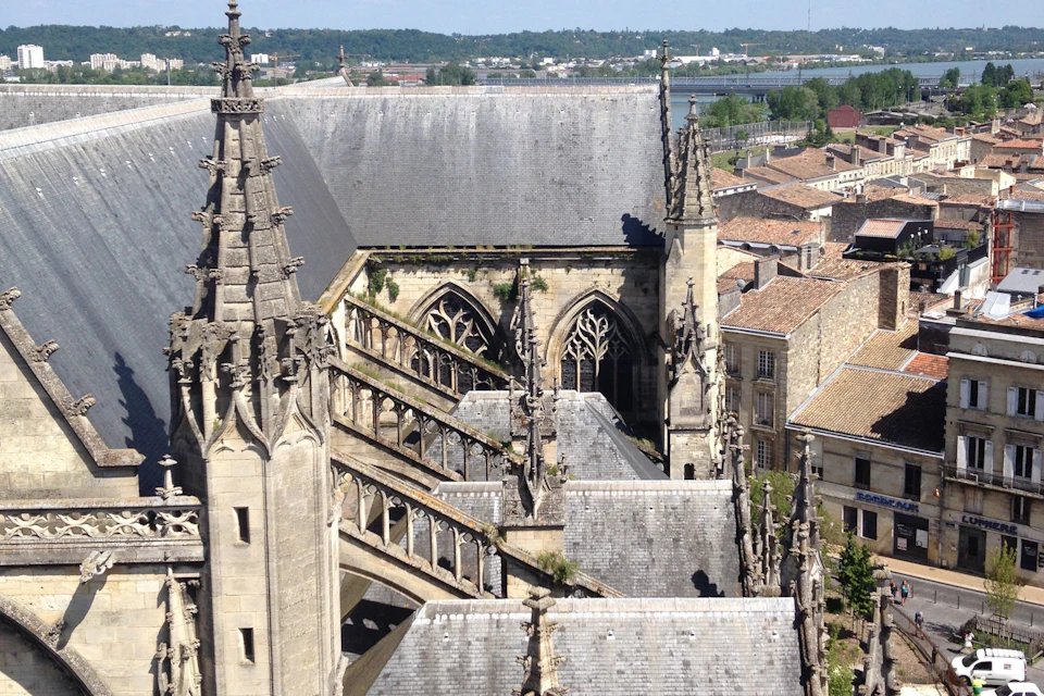 Aerial view of a Gothic church with flying buttresses, pointed arches, and surrounding buildings under a clear sky.