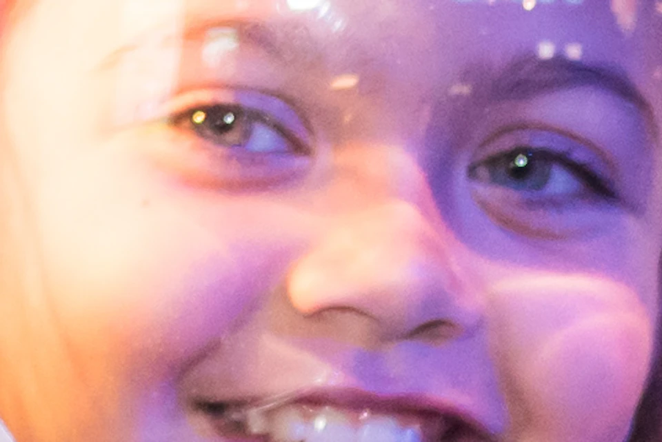 Child smiling inside a large astronaut suit at a space-themed exhibit with colorful lights in the background.