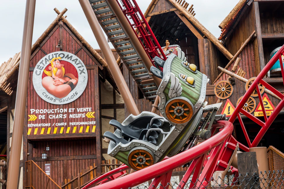 A theme park rollercoaster car designed with a medieval aesthetic, on a red track, with wooden buildings in the background.